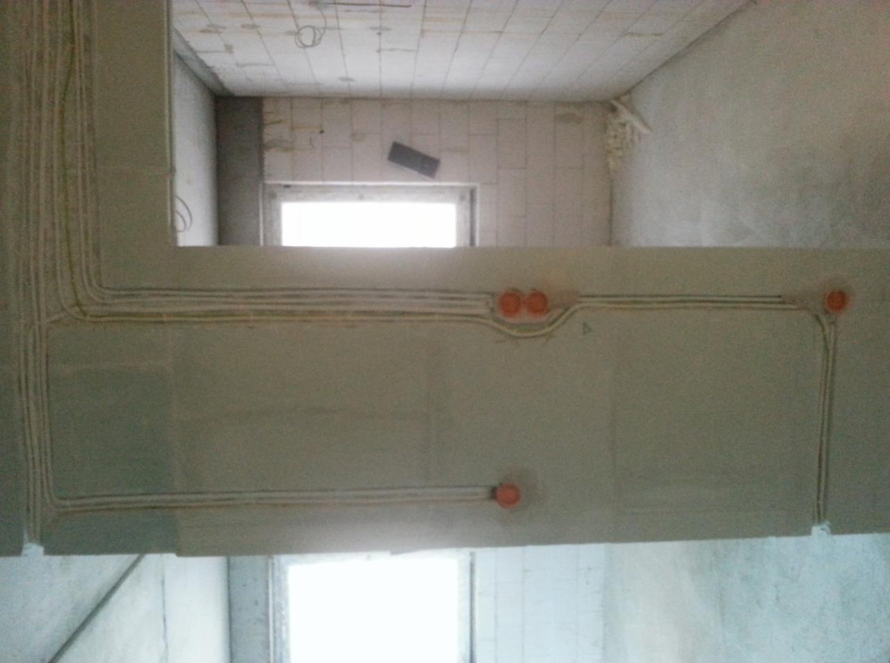 Surowe wnętrze w trakcie remontu z widocznymi przewodami elektrycznymi ułożonymi w bruzdach na ścianie i suficie, przygotowanymi do osadzenia gniazdek.