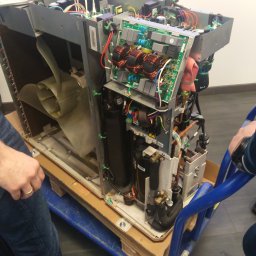 Hydrovolt Serwis - Otwarta obudowa klimatyzatora na wózku transportowym, widoczne elementy wewnętrzne: wentylator, sprężarka, elektronika. Serwis klimatyzacji w trakcie naprawy.