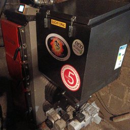 Hydrovolt Serwis - Kocioł grzewczy na paliwo stałe z oznaczeniami klasy 5 i EcoDesign, widoczny w kotłowni z ceglaną ścianą. Na kotle naklejki informacyjne i logo producenta.