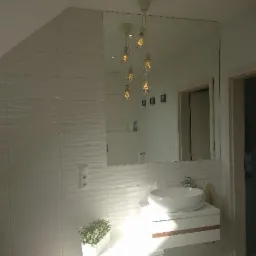 Nowoczesna łazienka z dużym lustrem na ścianie z białych płytek, wisząca szafka z umywalką i designerskie lampy wiszące z żarówkami Edisona.