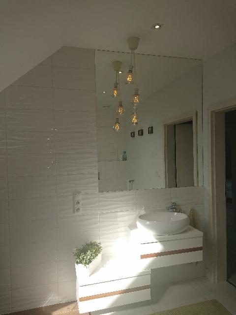 Nowoczesna łazienka z dużym lustrem na ścianie z białych płytek, wisząca szafka z umywalką i designerskie lampy wiszące z żarówkami Edisona.