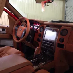 Wnętrze samochodu Ford F-150 po renowacji tapicerki, skórzane fotele z pikowaniem w romby, deska rozdzielcza i kierownica obszyte skórą w odcieniach brązu, widoczny kokpit i dźwignia zmiany biegów.