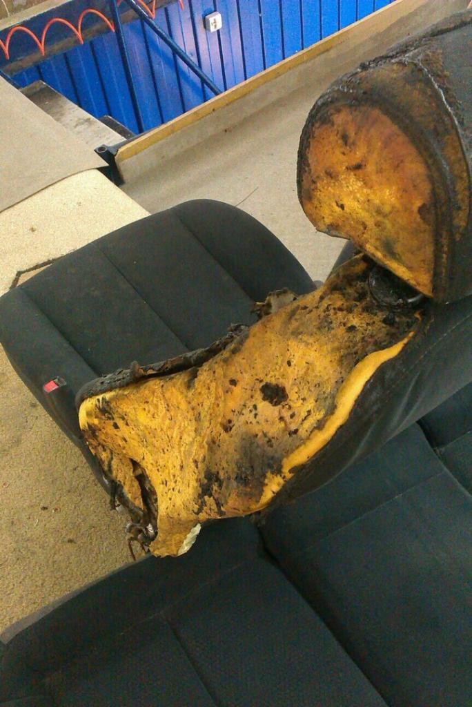 Zniszczone, rozerwane poszycie fotela samochodowego z widoczną, zbutwiałą gąbką, na tle drugiego fotela z ciemną tapicerką.