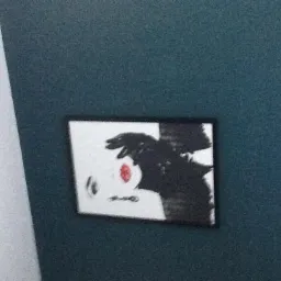 Ściana pomalowana na ciemny, morski odcień z wiszącym, oprawionym, czarno-białym obrazem z czerwonym akcentem.