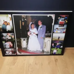 Duży, oprawiony w ramę kolaż zdjęć ślubnych, prezentujący różne momenty z uroczystości i wesela, ustawiony na podłodze.