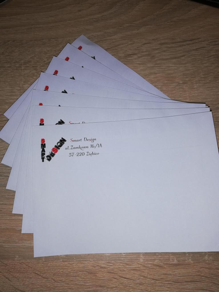 Stos wizytówek firmy Smart Design z adresem ul. Zamkowa 16/1A, 57-220 Ziębice, ułożonych na drewnianym blacie