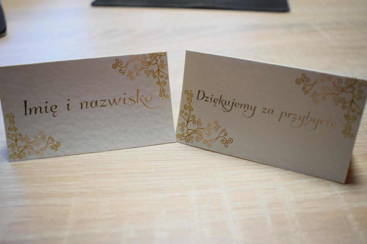Dwie kartki z podziękowaniami i miejscem na imię i nazwisko, zdobione złotymi ornamentami w rogach, leżące na drewnianym stole.