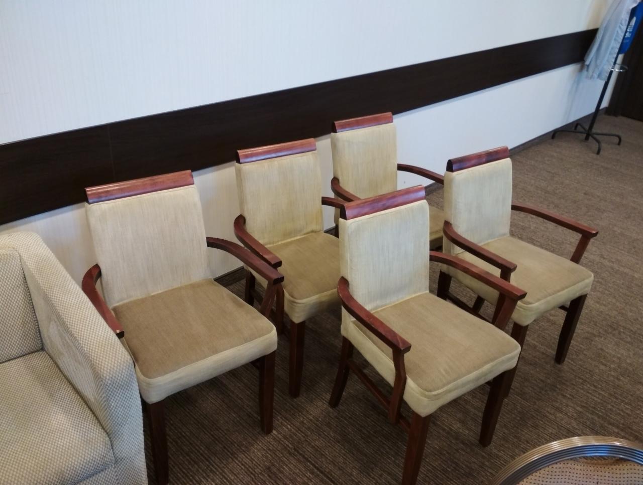 Pięć krzeseł z drewnianymi ramami i beżowymi obiciami, ustawionych w rzędzie obok sofy w pomieszczeniu z wykładziną dywanową.