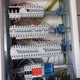 Rozdzielnica elektryczna w trakcie montażu, widoczne zabezpieczenia EATON, przewody w różnych kolorach i niebieskie złączki kablowe.