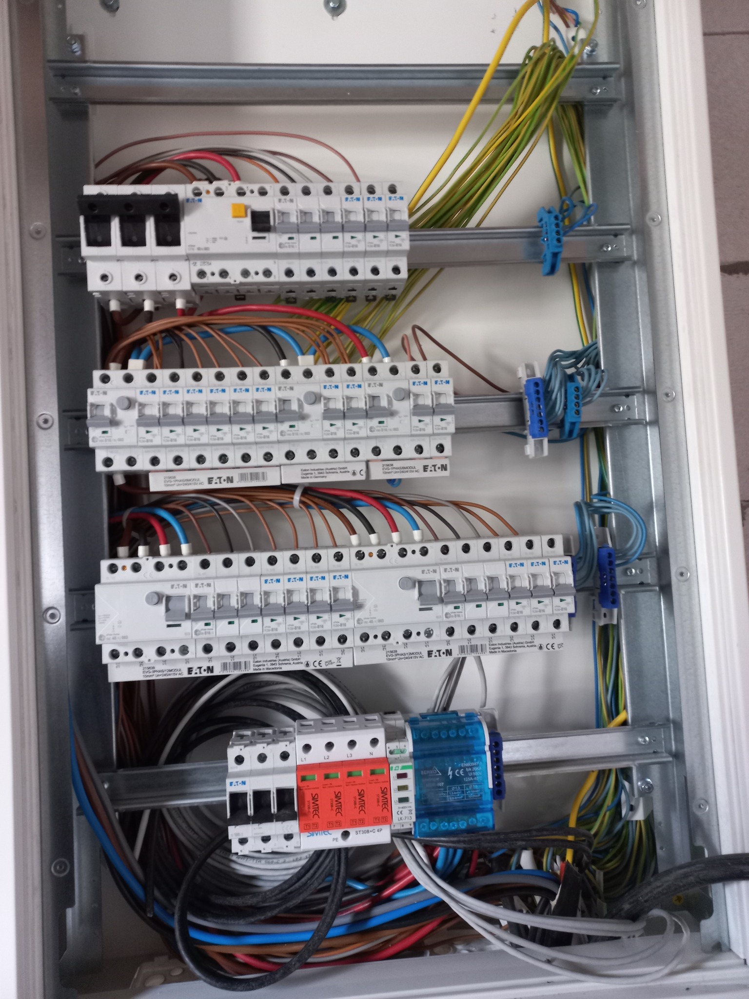 Rozdzielnica elektryczna w trakcie montażu, widoczne zabezpieczenia EATON, przewody w różnych kolorach i niebieskie złączki kablowe.