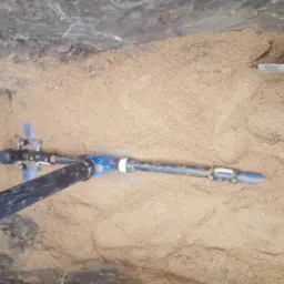 Rura wodociągowa z niebieskimi elementami złącznymi ułożona w wykopie zasypanym piaskiem, widoczny fragment szpadla.