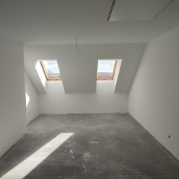 RK ELKO Knopik Rafał - Wnętrze poddasza po malowaniu na biało, z dwoma oknami dachowymi i szarą podłogą. Widoczne gładkie ściany i sufit, przygotowane do dalszych prac wykończeniowych.