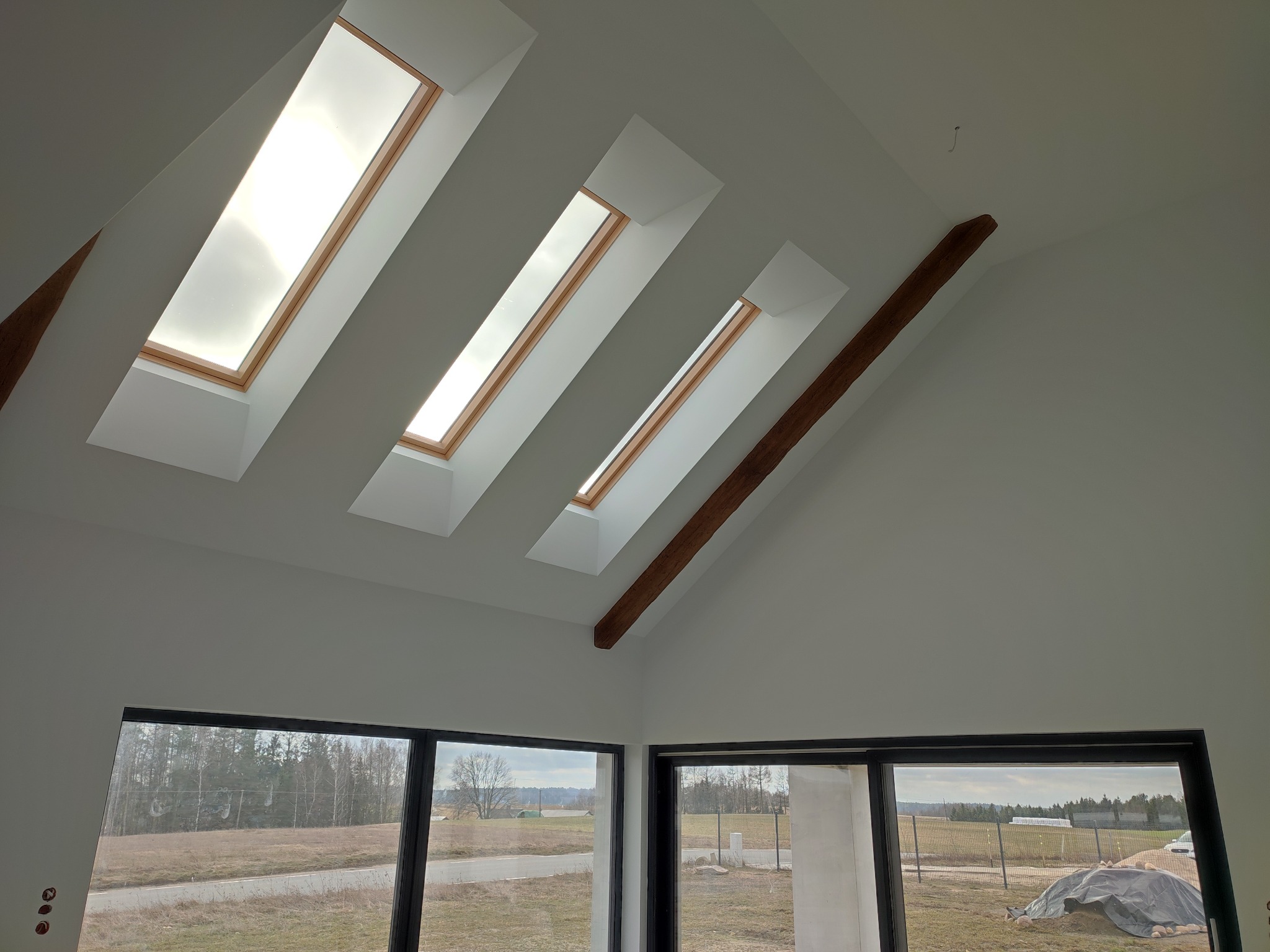 Jasne wnętrze w Lipusz z trzema oknami dachowymi i drewnianą belką stropową, widok z dołu na białe ściany i okna z widokiem na zewnątrz.