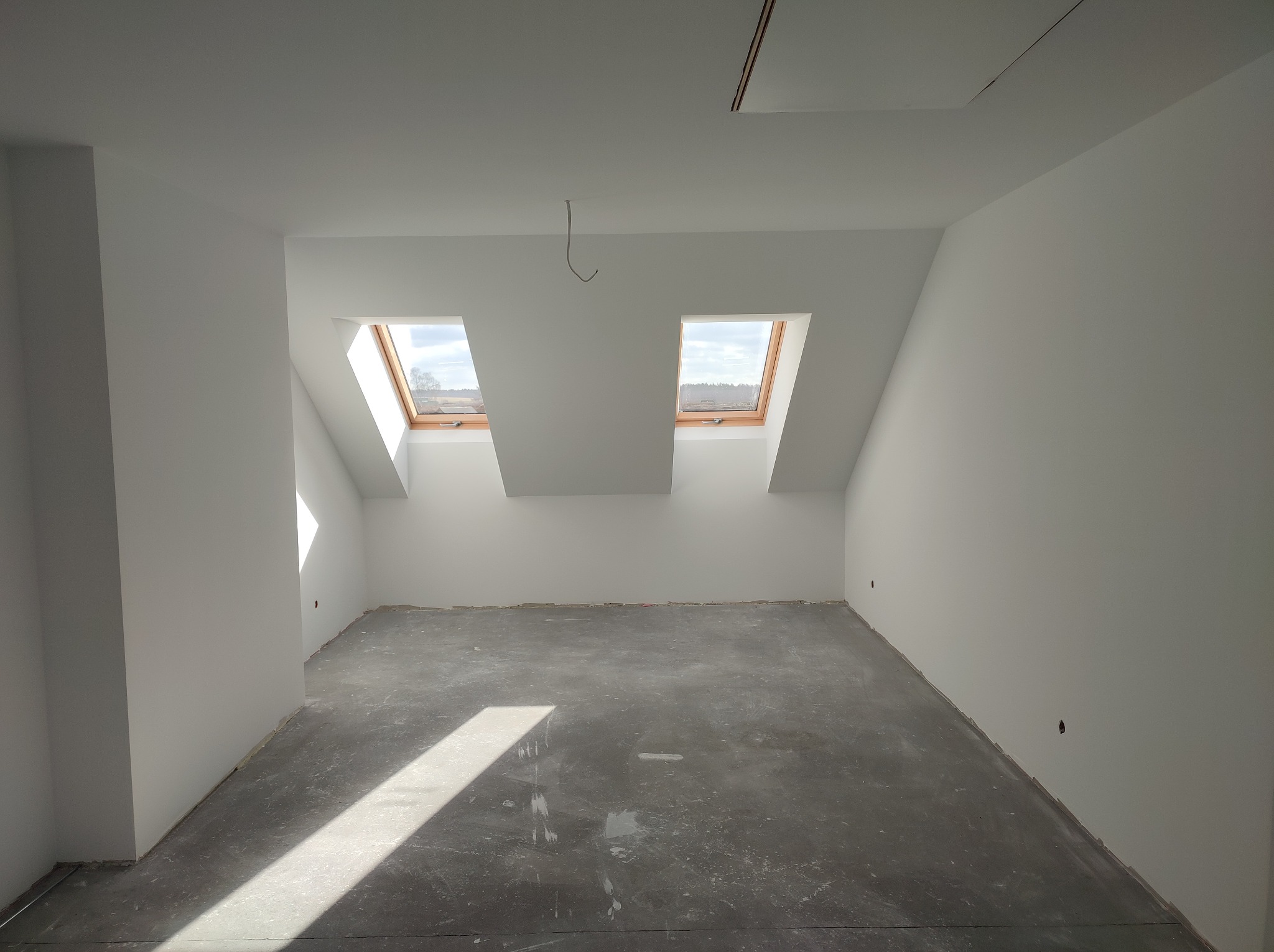 Wnętrze poddasza po malowaniu na biało, z dwoma oknami dachowymi i szarą podłogą. Widoczne gładkie ściany i sufit, przygotowane do dalszych prac wykończeniowych.