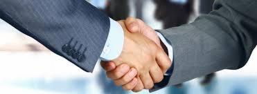 Uścisk dłoni dwóch mężczyzn w garniturach na rozmytym tle biurowym.