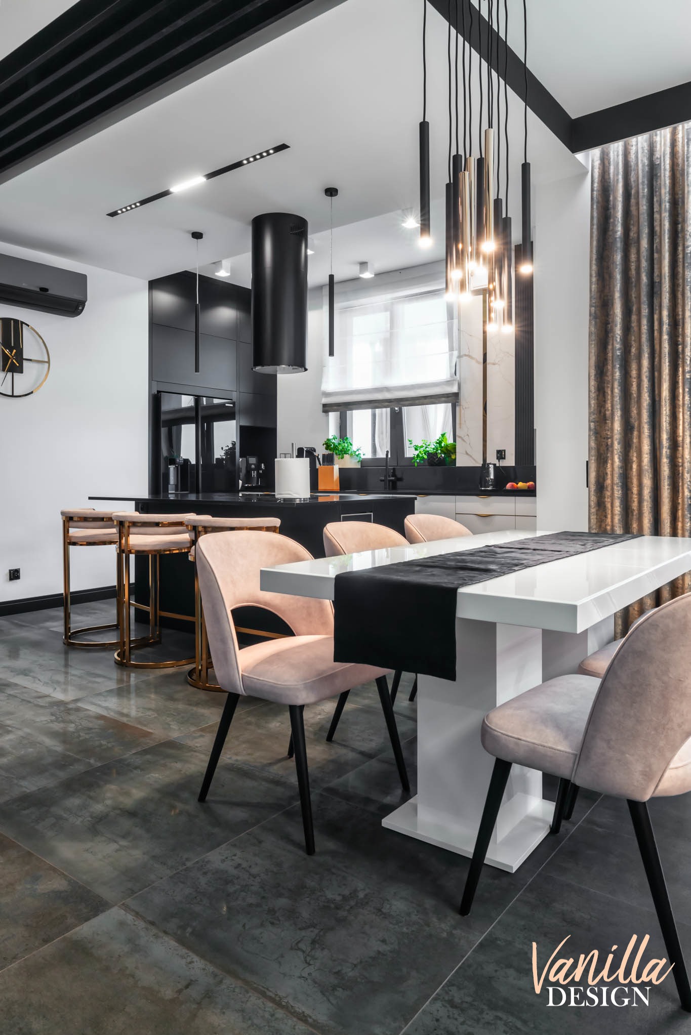 Nowoczesna jadalnia z białym stołem, różowymi krzesłami i czarnymi akcentami, w tym lampami wiszącymi i okapem kuchennym.