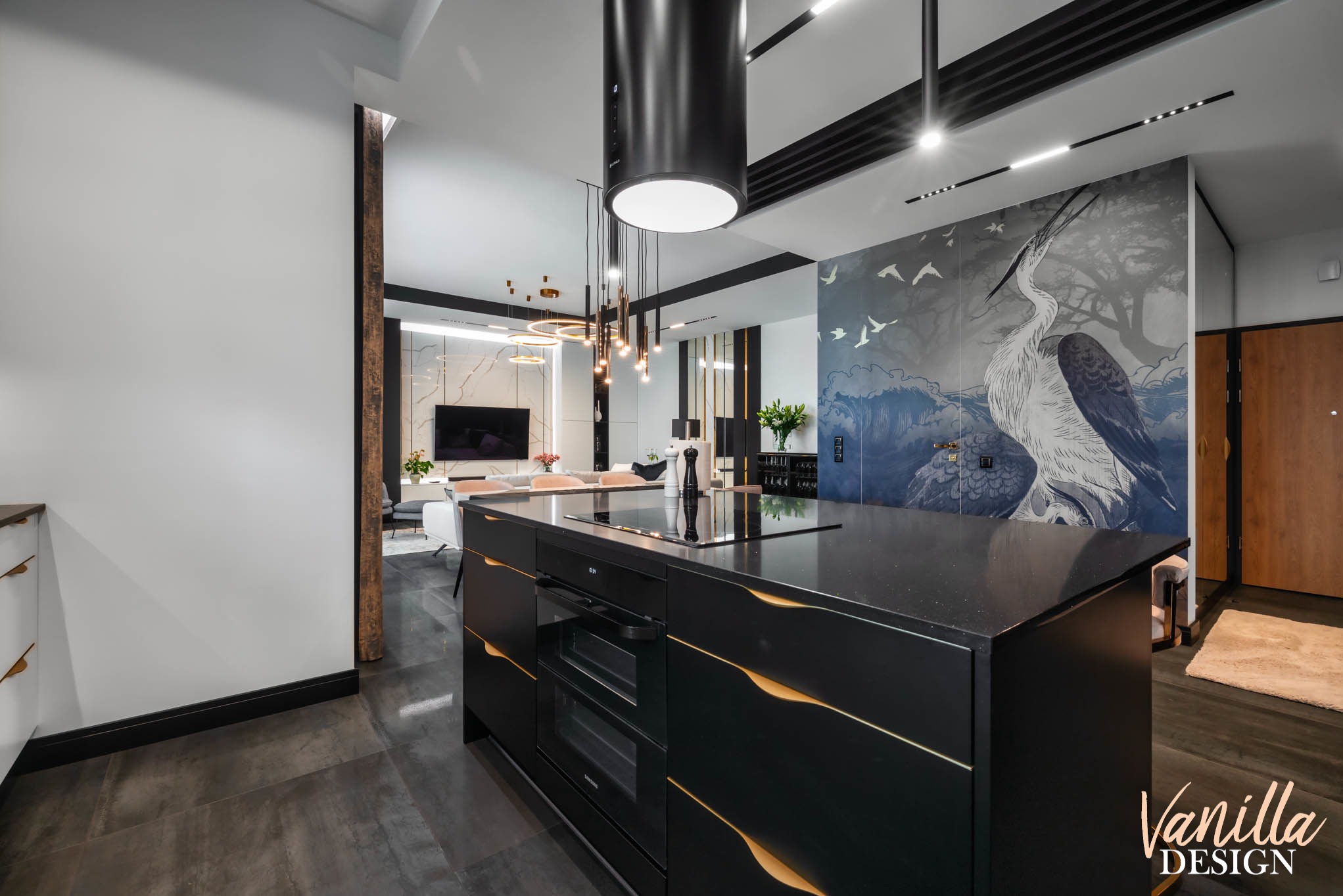 Czarne szafki kuchenne z dekoracyjnymi, złotymi wykończeniami, na tle salonu z tapetą przedstawiającą czaplę i nowoczesnym oświetleniem.
