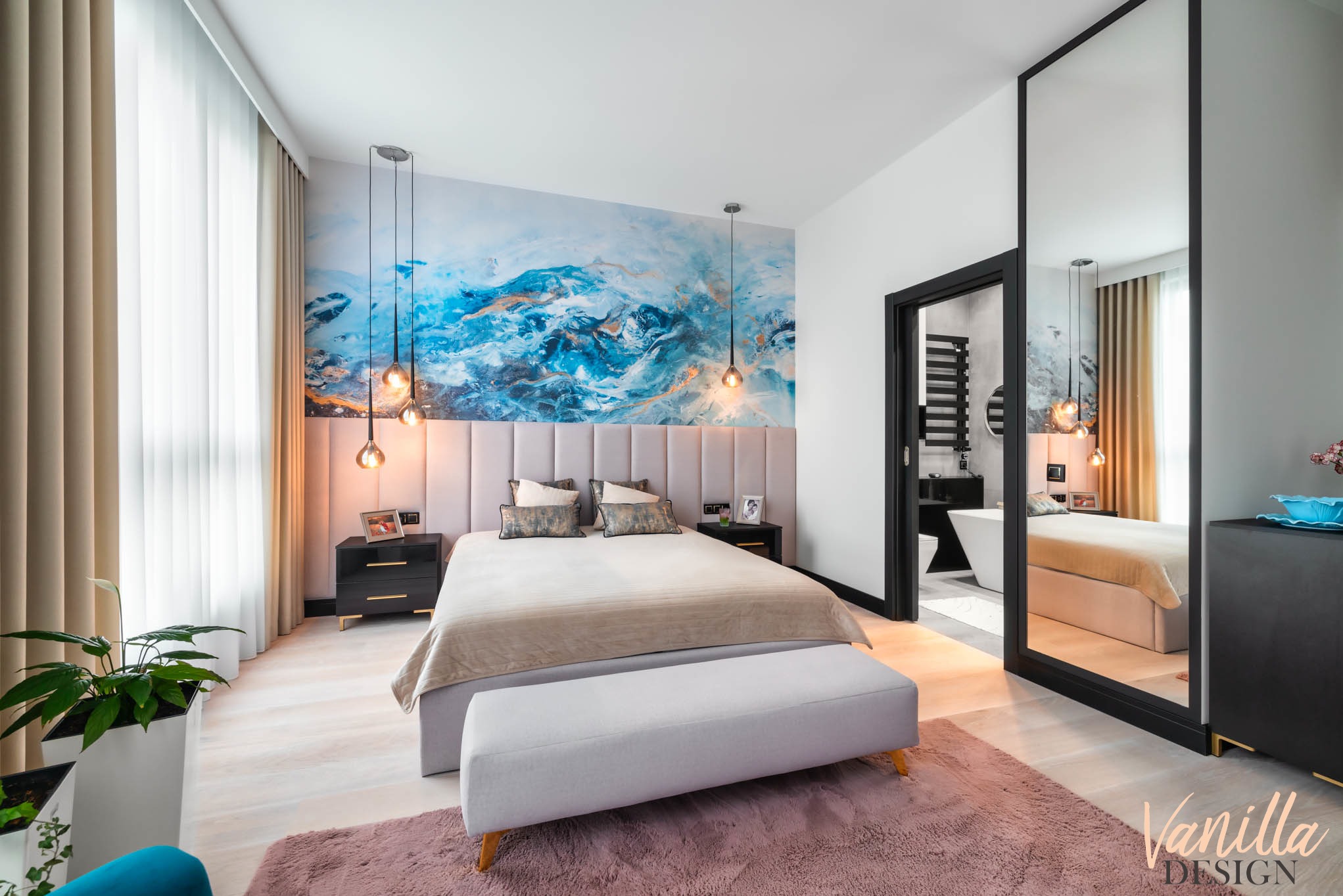 Nowoczesna sypialnia z łóżkiem kontynentalnym, tapetą z motywem abstrakcyjnym w odcieniach błękitu i złota, wiszącymi lampami w stylu industrialnym oraz widokiem na łazienkę przez otwarte drzwi.
