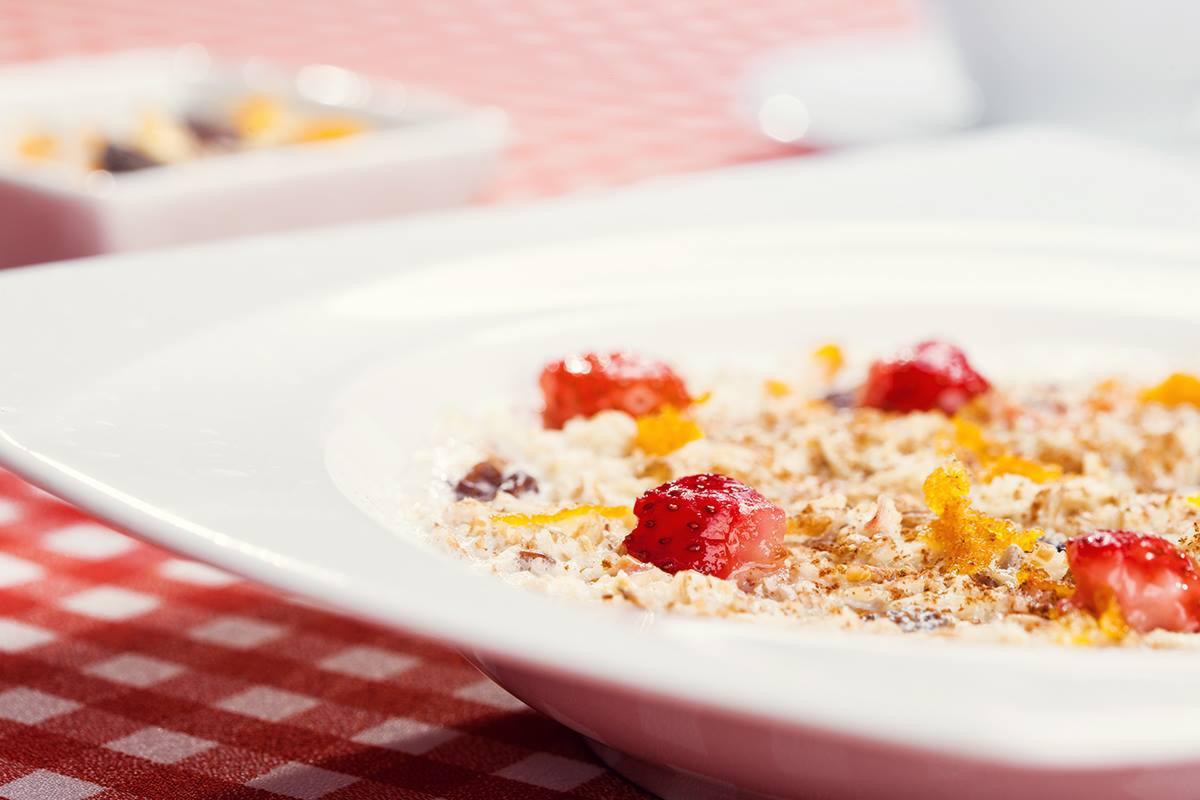 Owsianka z truskawkami i skórką pomarańczową w białym talerzu na czerwono-białym obrusie w kratę, widok z bliska.