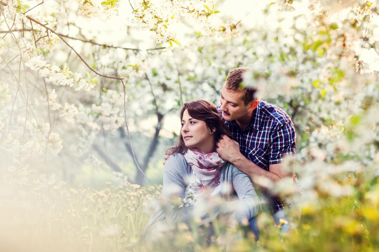 Para zakochanych w kwitnącym sadzie, mężczyzna obejmuje kobietę, ona patrzy w dal, wiosenna atmosfera.