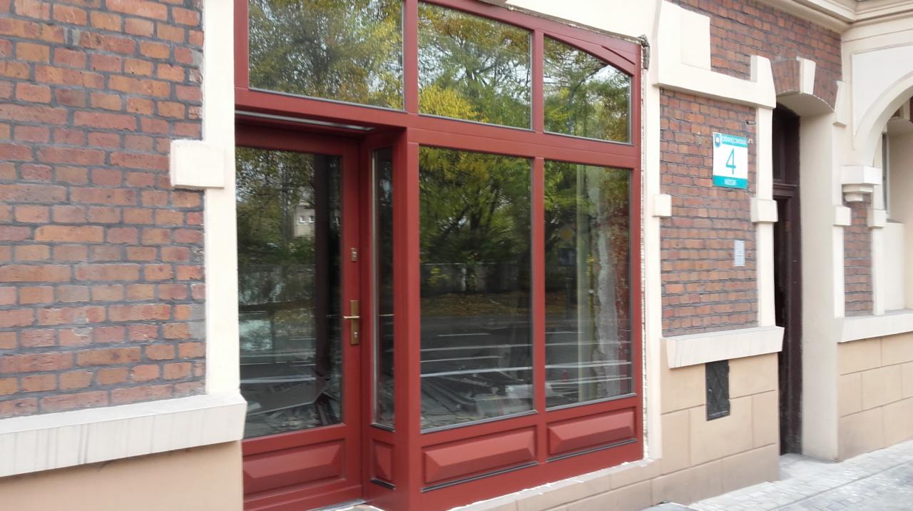 Czerwona stolarka okienna z drzwiami wejściowymi w budynku z cegły, widok z zewnątrz, z odbiciem drzew w szybach.
