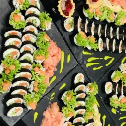 Sushi z łososiem i sałatą oraz mini tartaletki z dżemem na czarnych, matowych deskach z dodatkiem imbiru i zielonego sosu.