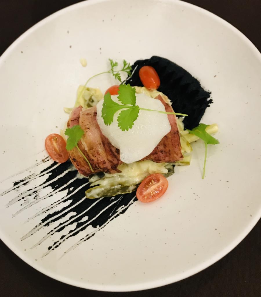 Elegancko podane danie z grillowaną polędwicą, pianką, pomidorkami cherry i czarną pastą na białym talerzu z artystycznymi smugami.