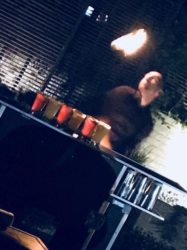 Barman przygotowuje kolorowe drinki na przenośnym barze podczas imprezy plenerowej, oświetlonej lampami.