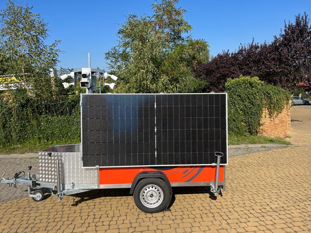 Mobilny system monitoringu: przyczepa z panelem solarnym i zestawem kamer na maszcie, na tle zieleni i błękitnego nieba. Nowoczesne rozwiązanie dla zabezpieczenia terenu.