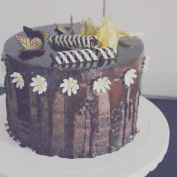 Czekoladowy tort z polewą, dekorowany białymi kwiatkami, czekoladowymi rulonikami i motylkiem, wykonany w Łodzi.