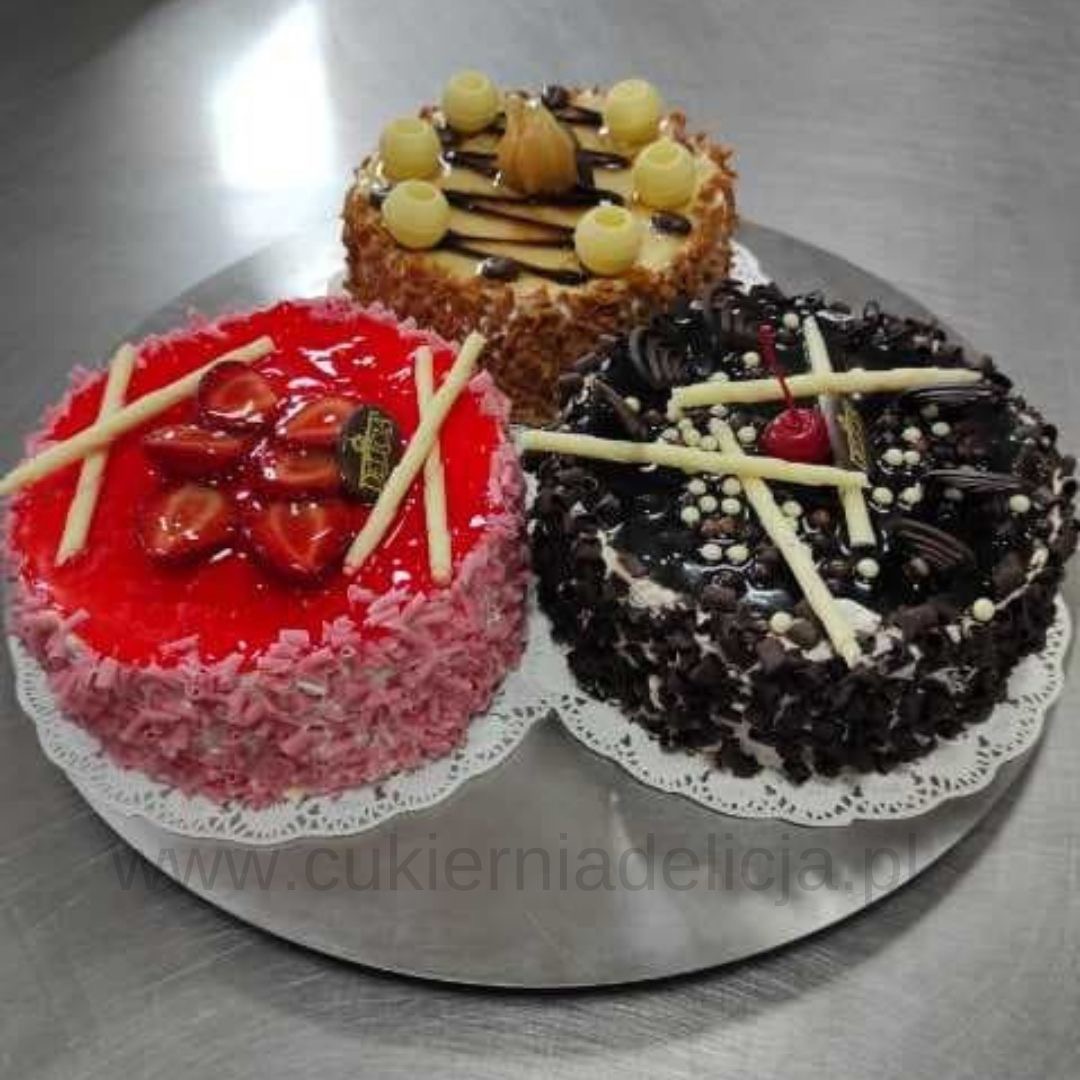 Trzy okrągłe torty na srebrnej tacy: truskawkowy z czerwoną galaretką i różowymi wiórkami, czekoladowy z polewą, mini kuleczkami i wiśnią, oraz orzechowy z kremowymi kulkami i polewą.