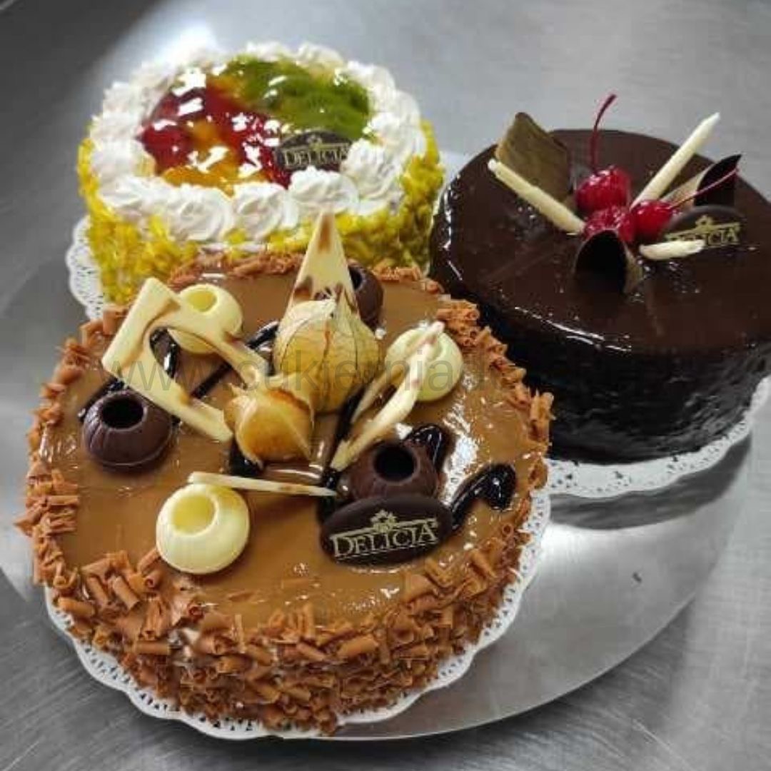 Trzy torty na srebrnej tacy: tort z galaretką owocową i bitą śmietaną, tort karmelowy z dekoracjami z białej i ciemnej czekolady oraz tort czekoladowy z wiśniami i czekoladowymi dekoracjami.