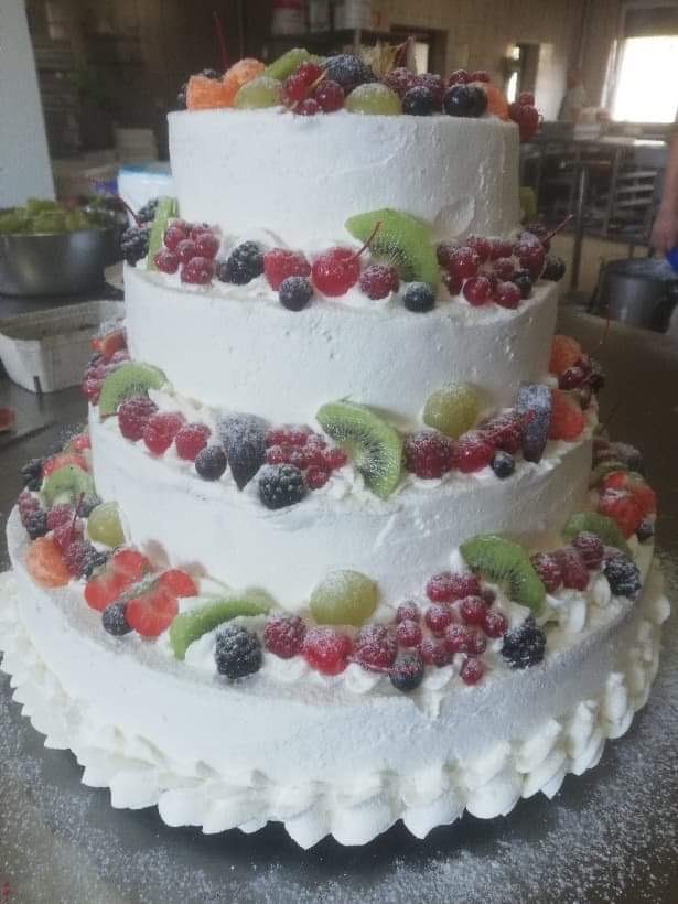Trzypiętrowy tort weselny z białym kremem, udekorowany świeżymi owocami: kiwi, czerwonymi porzeczkami, malinami, jeżynami i winogronami, posypany cukrem pudrem.