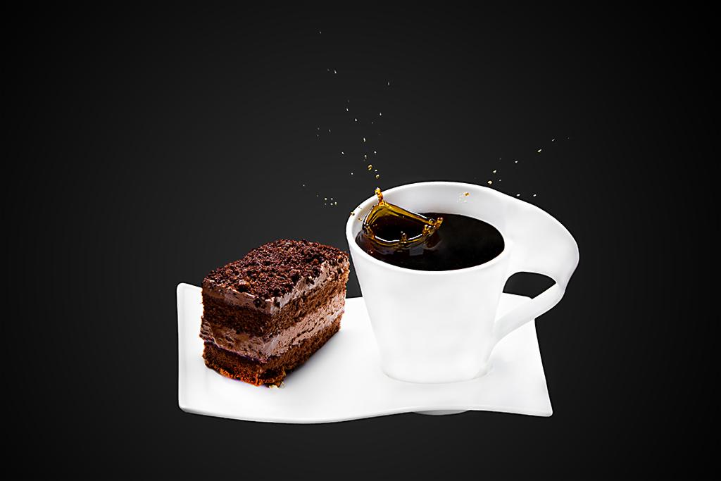 Kawa w białym kubku z kroplą i kawałek czekoladowego tortu na białym talerzyku, czarne tło.