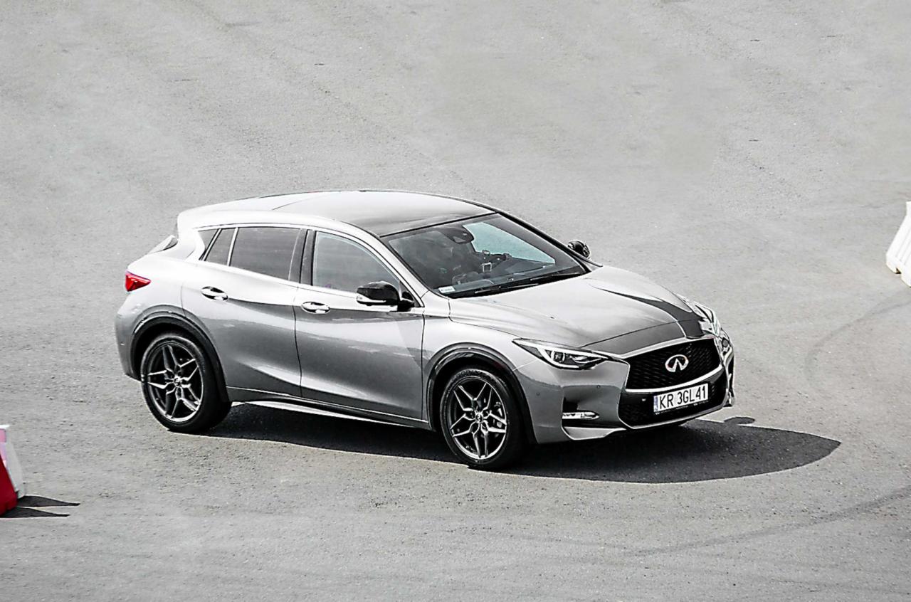 Szary crossover Infiniti Q30 z czarnym pasem na masce, zaparkowany na szarym asfalcie, widok z góry.