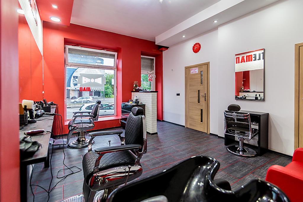 Wnętrze salonu fryzjerskiego z trzema skórzanymi fotelami barberskimi, stanowiskiem z lustrem i narzędziami, czerwonymi ścianami i elementami dekoracyjnymi.