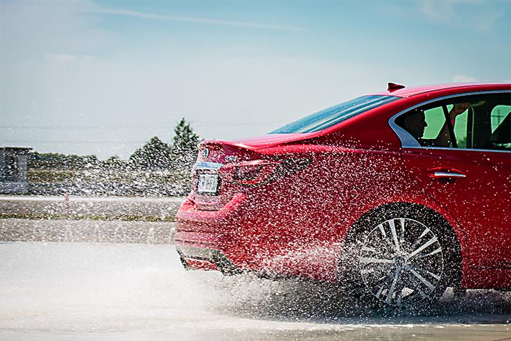 Czerwony samochód w ruchu, tylny widok, rozpryskująca się woda spod kół, dynamiczne ujęcie na mokrej nawierzchni.