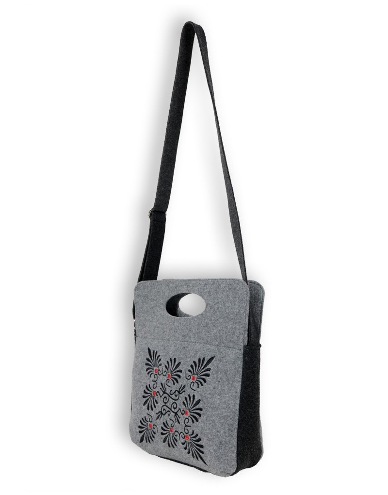 Szara filcowa torba na ramię z czarno-czerwonym haftowanym wzorem kwiatowym, wisząca na białym tle.