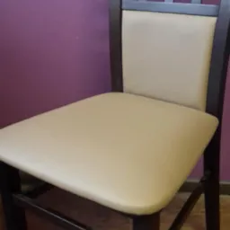 Krzesło z ciemnego drewna z beżową tapicerką siedziska i oparcia, na tle fioletowej ściany, z charakterystyczną kratką w oparciu.