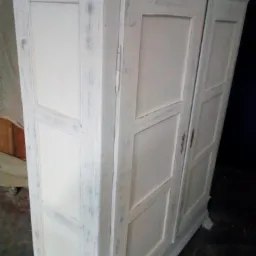 Dwudrzwiowa szafa drewniana w stylu shabby chic, malowana na biało z efektem postarzenia, widoczne metalowe zawiasy i uchwyty.