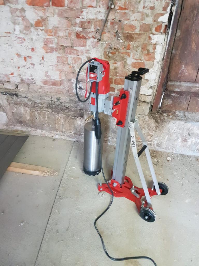 Wiertnica diamentowa Milwaukee DR 350 T na statywie, przygotowana do wiercenia rdzeniowego w ścianie z czerwonej cegły w surowym wnętrzu.