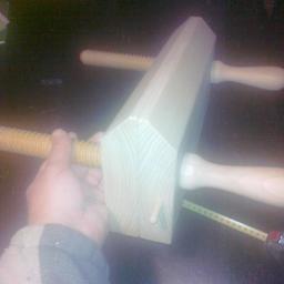 Amadeusz-Alina Krystel - Drewniany ścisk stolarski w dłoni, widoczny fragment miarki zwijanej, ciemne tło.