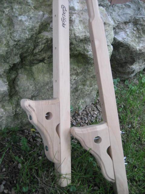 Dwa drewniane szczudła z widocznym logo 'Cwikliński' na jednym z nich, ustawione na trawie przed kamiennym tłem.