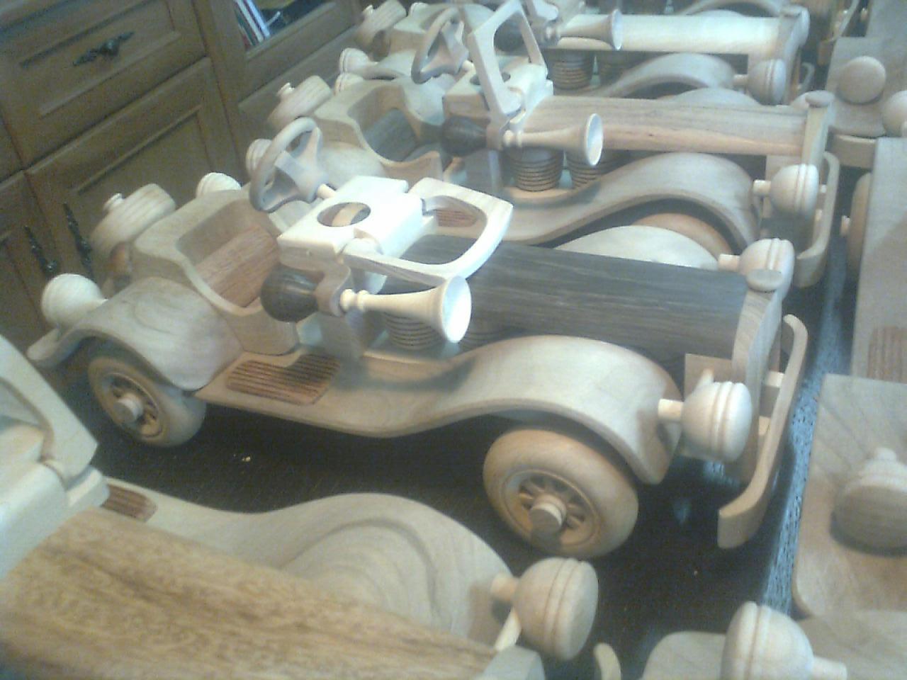 Ręcznie robione, drewniane modele zabytkowych samochodów, ustawione jeden za drugim, z widocznymi detalami takimi jak kierownice, koła i reflektory.