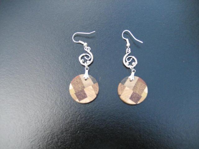 Para wiszących kolczyków z okrągłymi, drewnianymi elementami w mozaikę z kwadratów w odcieniach brązu i beżu, zawieszonych na srebrnych, spiralnych zaczepach.