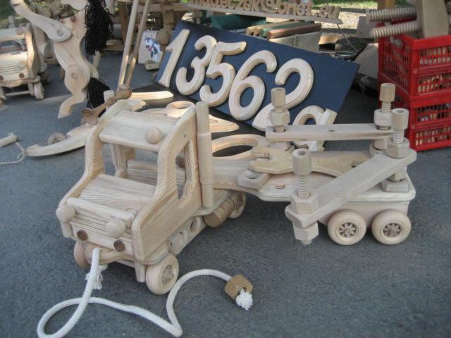 Drewniana zabawka - laweta z numerem '13562' w tle, wykonana z jasnego drewna, z widocznymi elementami skręcanymi śrubami i nakrętkami.