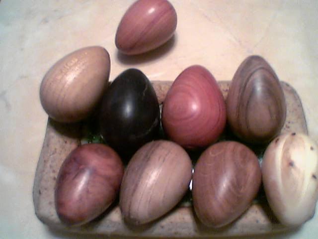 Kolekcja dziewięciu drewnianych jajek o różnych odcieniach brązu i czerni, ułożonych na kamiennej tacy.