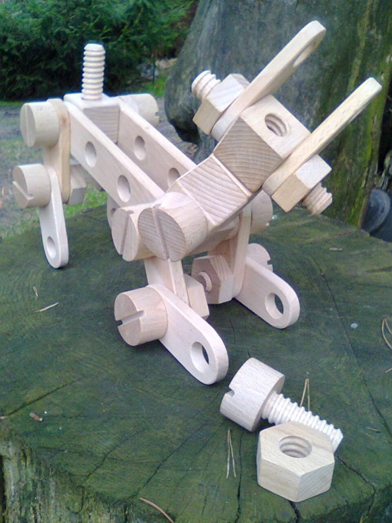 Drewniana zabawka edukacyjna przedstawiająca konstrukcję z nakrętek, śrub i łączników na tle pnia drzewa.