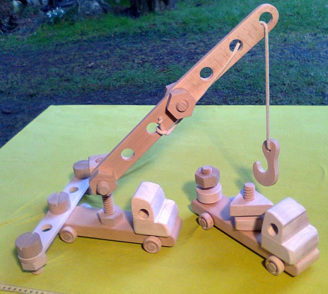 Dwa drewniane zestawy zabawek: dźwig z wysięgnikiem i dwie ciężarówki, wykonane z jasnego drewna, umieszczone na zielonym tle.