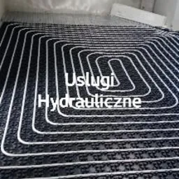 Rozłożone rury ogrzewania podłogowego na czarnej macie z wypustkami, widok z góry w surowym stanie, przed wylaniem posadzki.